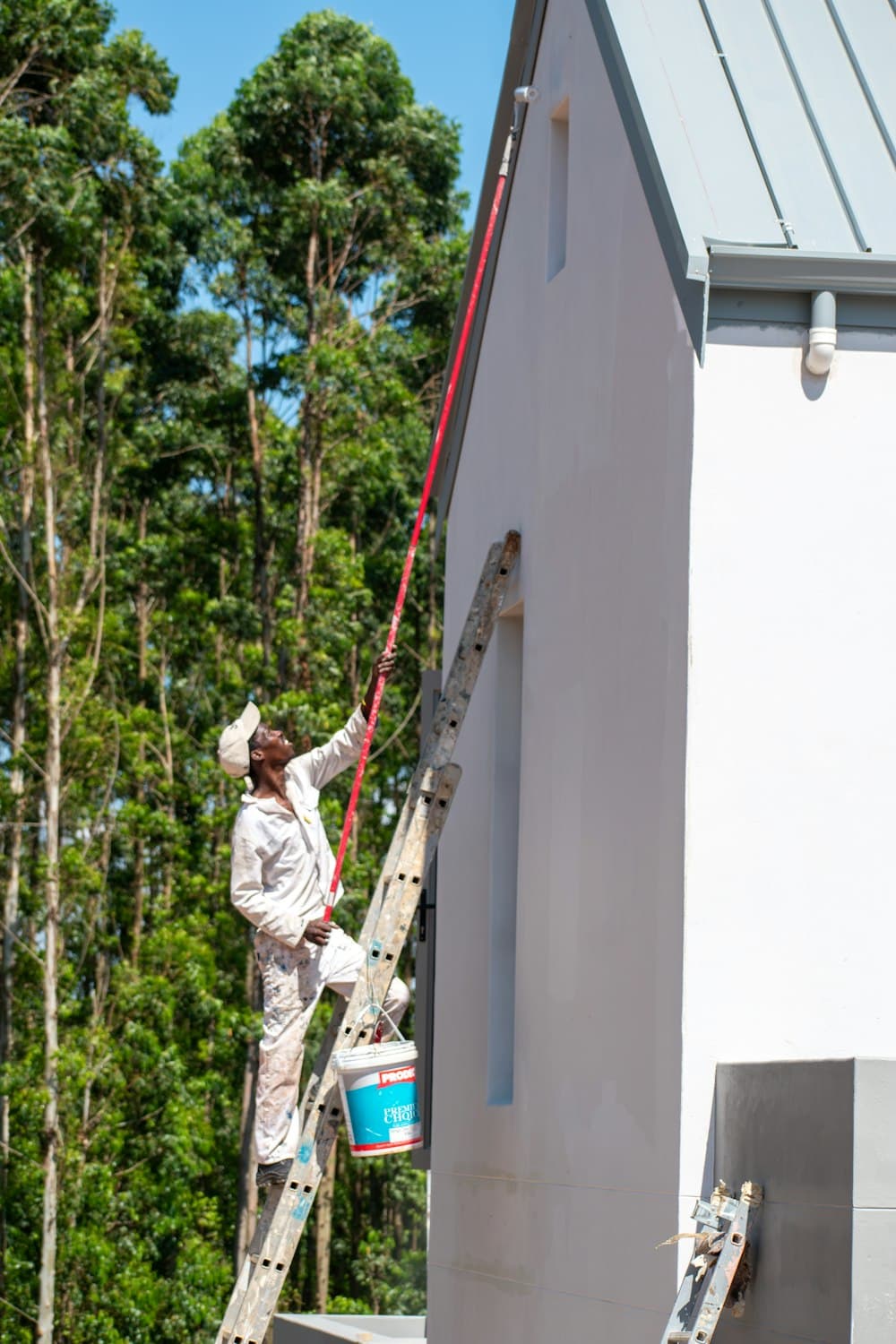 Painter on a ladder coating the exterior wall of a white house